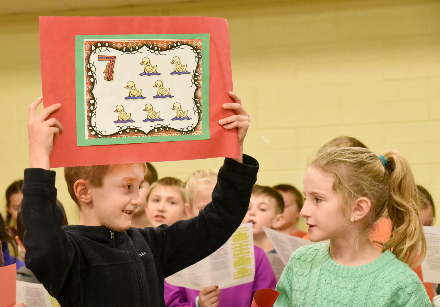 Liam Frederick holds up a poster for seven swans a swimming. He and Kinsley Ginerich were performing “The Twelve Days of Christmas.” The Mid-Prairie East second graders performed Christmas songs for the Rotary Club of Kalona on Dec. 17.